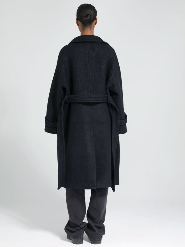 A model wearing a black oversized coat with a belt, showcasing a stylish and cozy design by MEOTINE from the back.