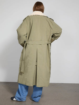 A model wearing a long olive green coat with a fluffy collar, styled with loose blue jeans, showcasing MEOTINE's chic design.