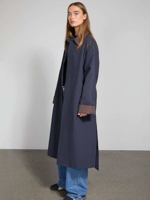 A model showcases a stylish navy blue long coat with contrasting brown cuffs, paired with relaxed denim jeans. MEOTINE.