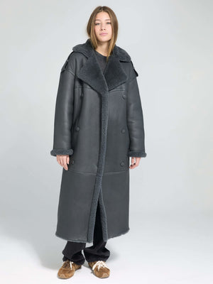 A model wearing a long, gray MEOTINE coat with a plush collar, styled with a casual black outfit and brown shoes.