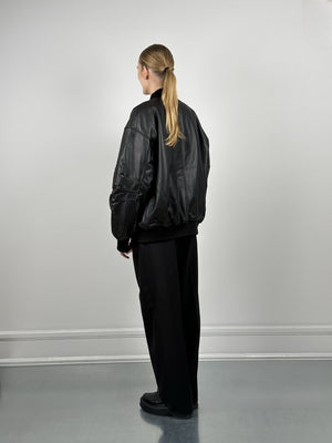 A model wearing a black oversized leather jacket from MEOTINE, paired with loose black trousers, viewed from the back.