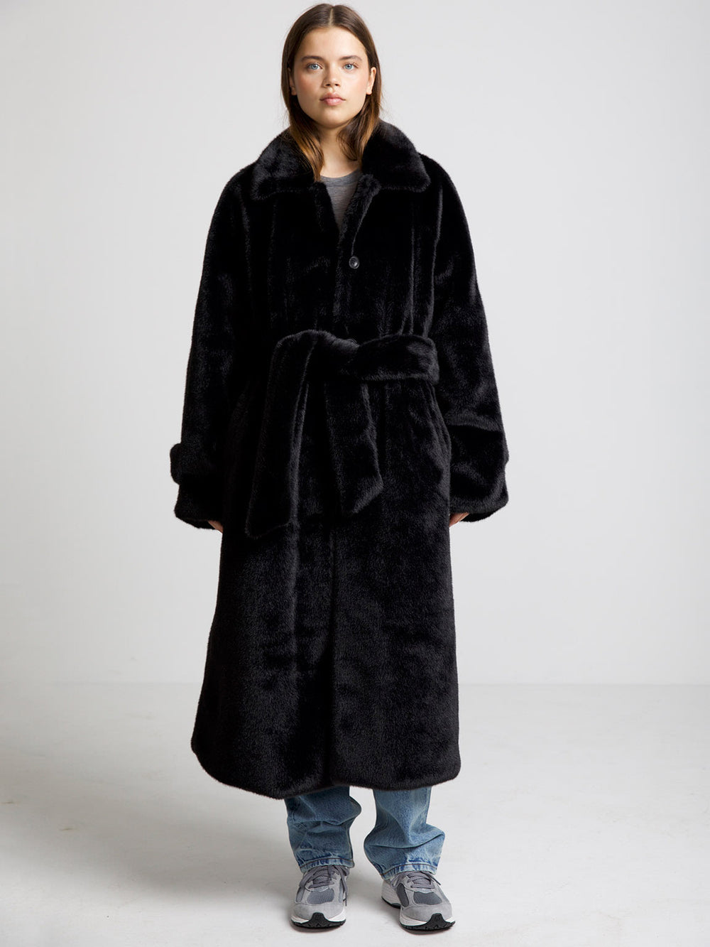 A model wears a cozy black faux fur coat with a belt, paired with casual jeans and sneakers, showcasing MEOTINE's stylish design.
