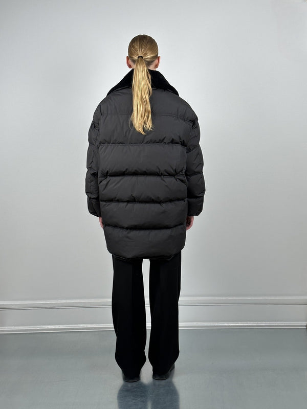 A model wearing a black oversized puffer jacket from MEOTINE, viewed from the back, paired with black wide-leg pants.
