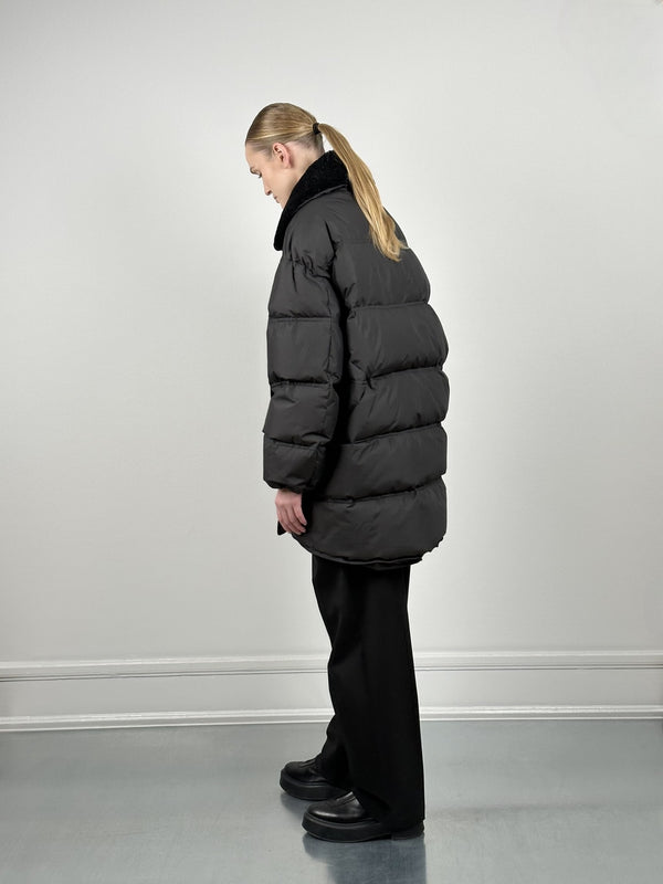 A model wearing a black puffer coat with a fur collar, styled with loose black pants and chunky boots, showcasing MEOTINE's winter collection.