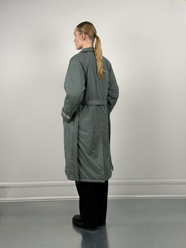 A model showcases a stylish MEOTINE long coat in a muted green color, featuring a belted waist and a relaxed fit from the back.