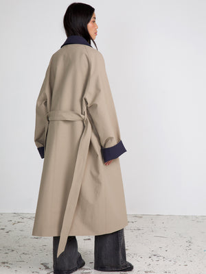 A model showcases a stylish beige trench coat with navy accents, featuring a belted waist and relaxed fit, by MEOTINE.