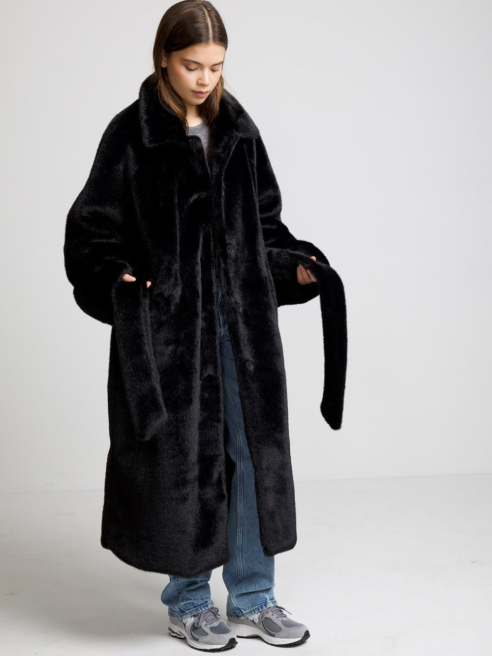 A model wears a cozy black faux fur coat with a belt, paired with casual jeans and sneakers, showcasing MEOTINE's stylish design.