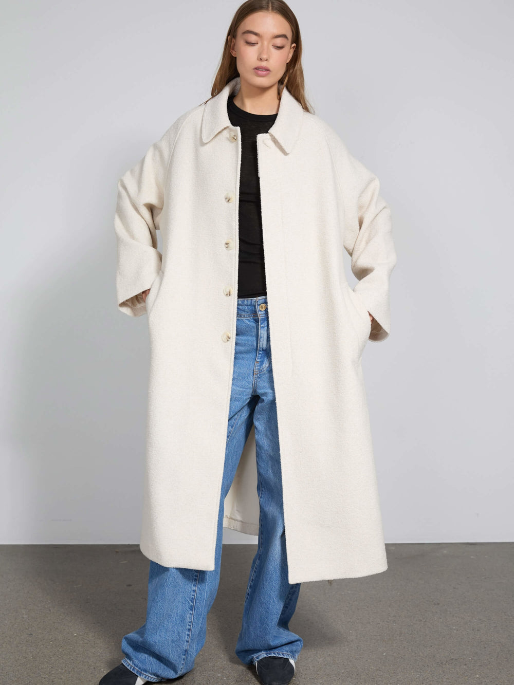 A model showcases a cozy, oversized cream coat by MEOTINE, paired with relaxed blue jeans and a simple black top.
