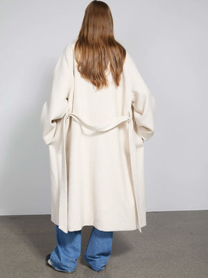 A model wearing a cozy, cream-colored MEOTINE coat with a relaxed fit, styled with blue jeans, showcasing a minimalist design.