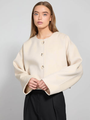 A model wears a cream-colored, oversized jacket with a round neckline and button closure, showcasing a stylish, modern look by MEOTINE.