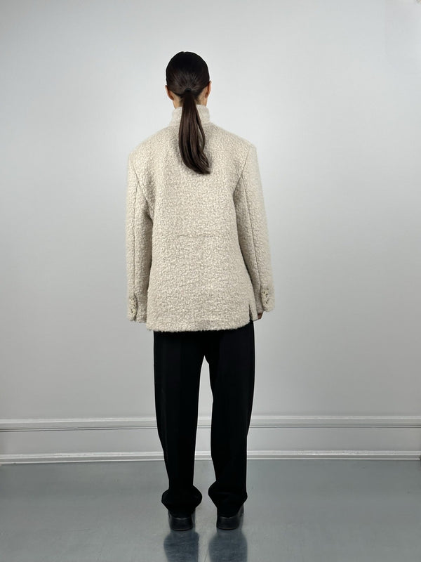 A model wearing a cozy, cream-colored MEOTINE jacket, paired with black trousers, seen from the back against a neutral backdrop.