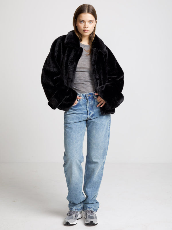 A model wears a cozy black faux fur jacket paired with a gray top and light blue jeans, showcasing MEOTINE's stylish design.