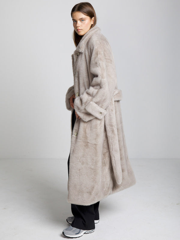 A model wearing a soft, oversized beige faux fur coat by MEOTINE, styled with black pants and sneakers against a neutral backdrop.