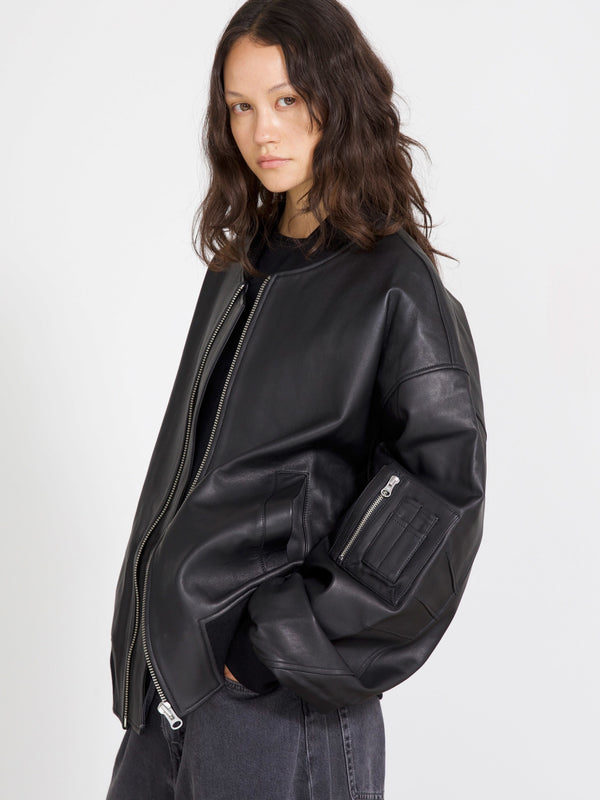 A model showcases a stylish black leather bomber jacket by MEOTINE, featuring a relaxed fit and zippered pockets.