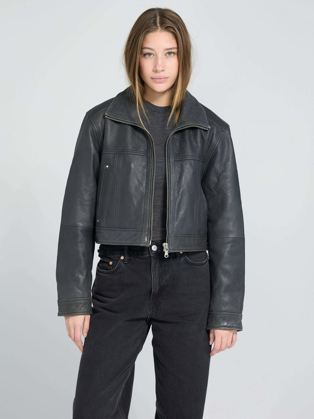A model wearing a stylish black cropped leather jacket from MEOTINE, paired with a simple black top and jeans.