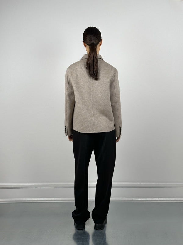 A model wearing a beige oversized blazer from MEOTINE, paired with black trousers, stands against a minimalist backdrop.