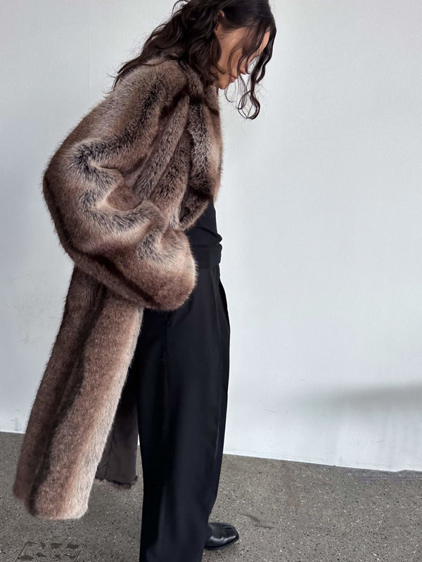 A model showcases a luxurious brown faux fur coat by MEOTINE, paired with black trousers, exuding elegance and style.