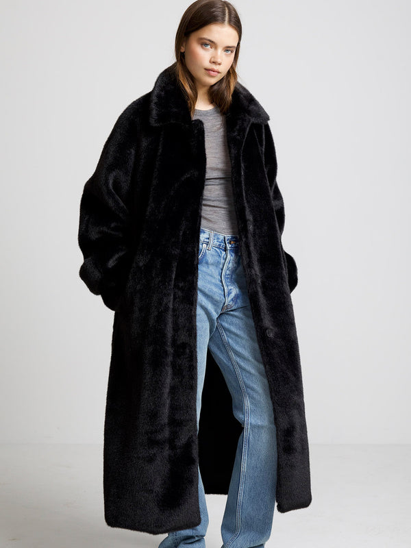 A model showcases a cozy black faux fur coat by MEOTINE, paired with a simple gray top and relaxed-fit jeans.