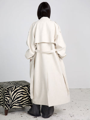A model wearing a stylish beige trench coat from MEOTINE, showcasing a relaxed fit and elegant design, stands against a neutral backdrop.