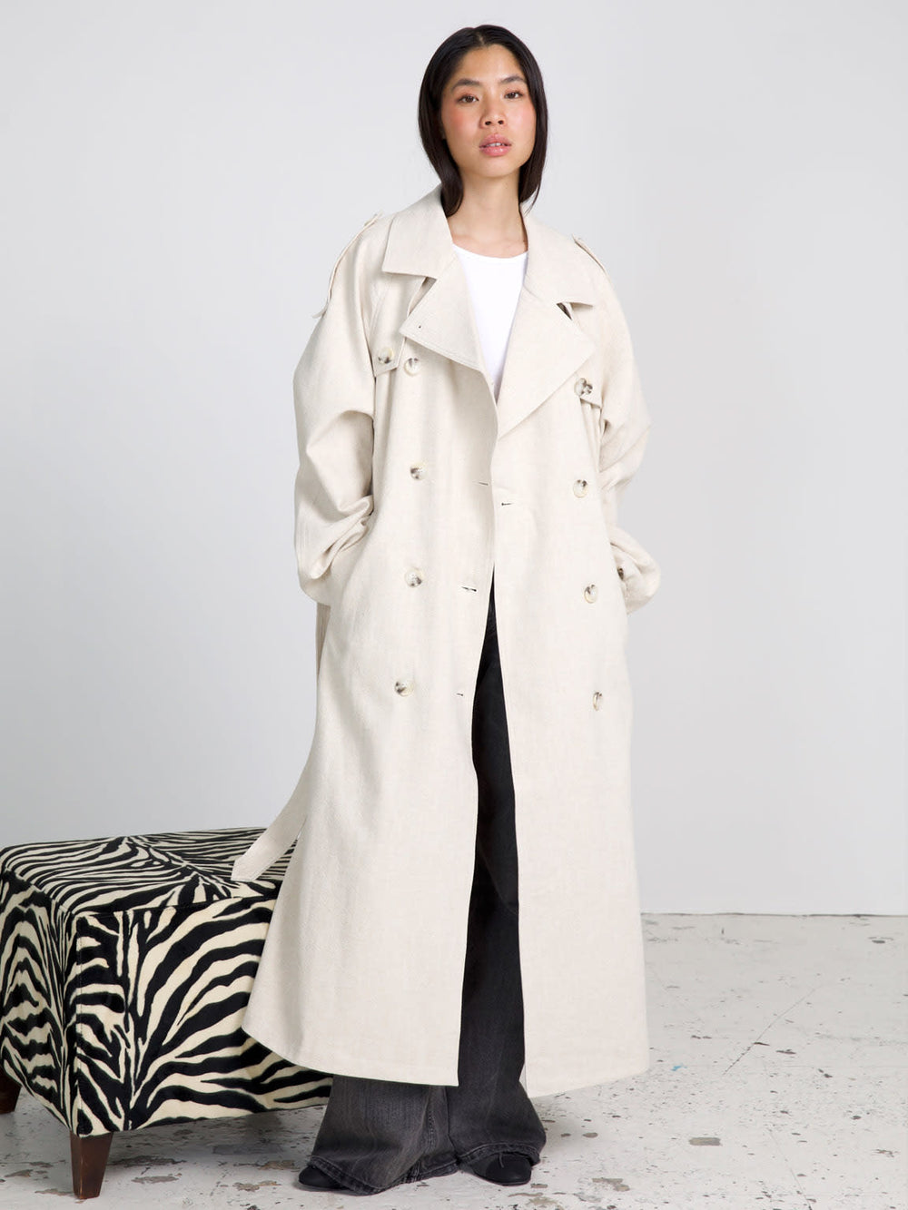 A model wears a stylish beige trench coat by MEOTINE, paired with wide-leg jeans, showcasing a chic and modern look.