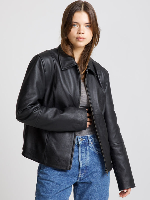A model wears a stylish black leather jacket from MEOTINE, paired with a gray top and blue jeans, showcasing a modern look.