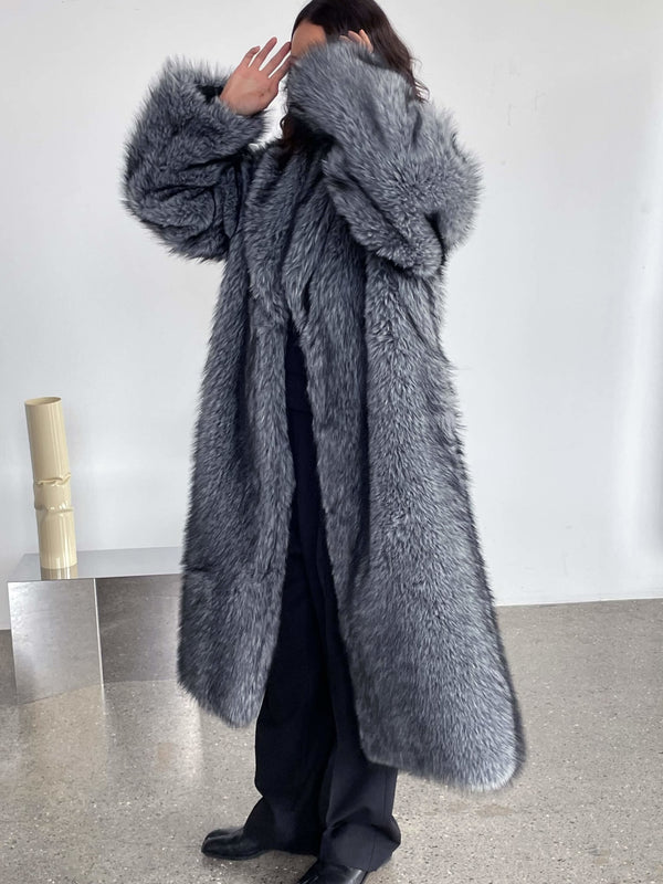 A model wearing a luxurious gray faux fur coat by MEOTINE, styled with black pants, poses against a minimalist backdrop.