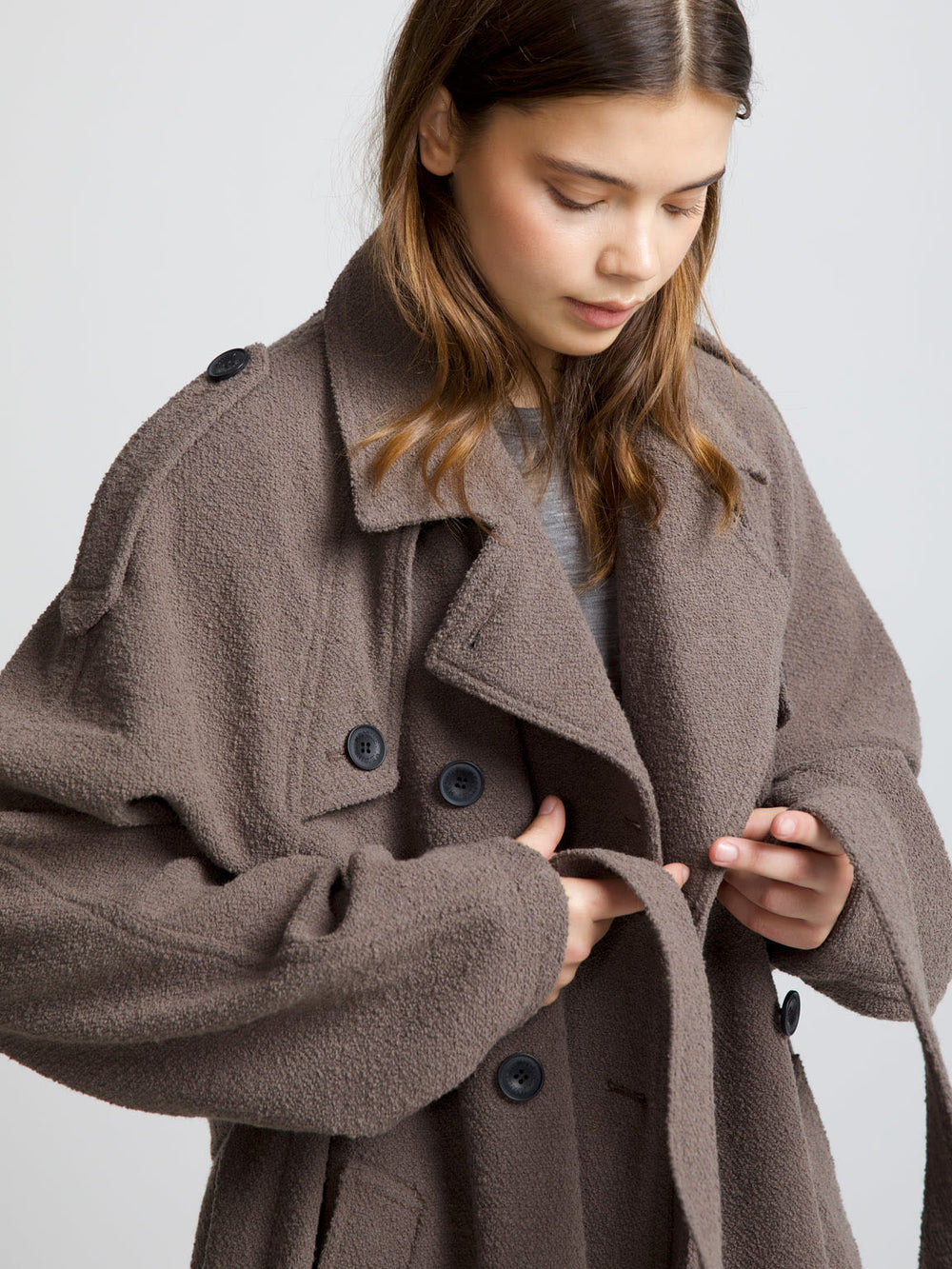 A model wears a long, oversized brown coat with a double-breasted design, styled with casual jeans and sneakers by MEOTINE.