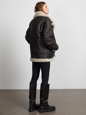 A model showcases a stylish black leather jacket with a cozy cream shearling collar, paired with sleek black leggings and tall boots.