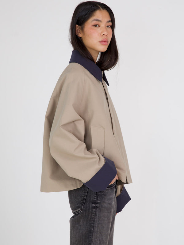 A model showcases a stylish beige and navy jacket by MEOTINE, featuring a relaxed fit and modern design, paired with dark jeans.