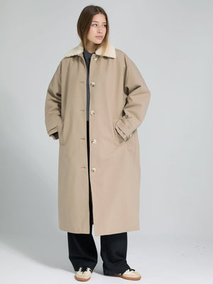 A model wears a beige oversized coat with a soft collar, styled with black pants and sneakers, showcasing MEOTINE's cozy design.