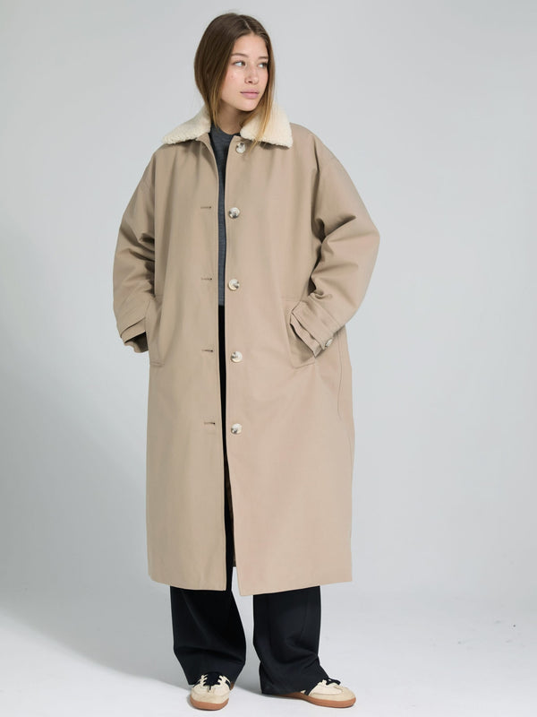 A model wears a beige oversized coat with a soft collar, styled with black pants and sneakers, showcasing MEOTINE's cozy design.