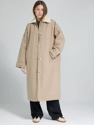 A model wears a beige oversized coat with a soft collar, styled with black pants, showcasing MEOTINE's chic outerwear design.