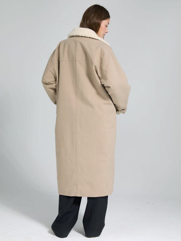 A woman in a beige oversized coat with a fluffy collar, showcasing a stylish and cozy look from MEOTINE.