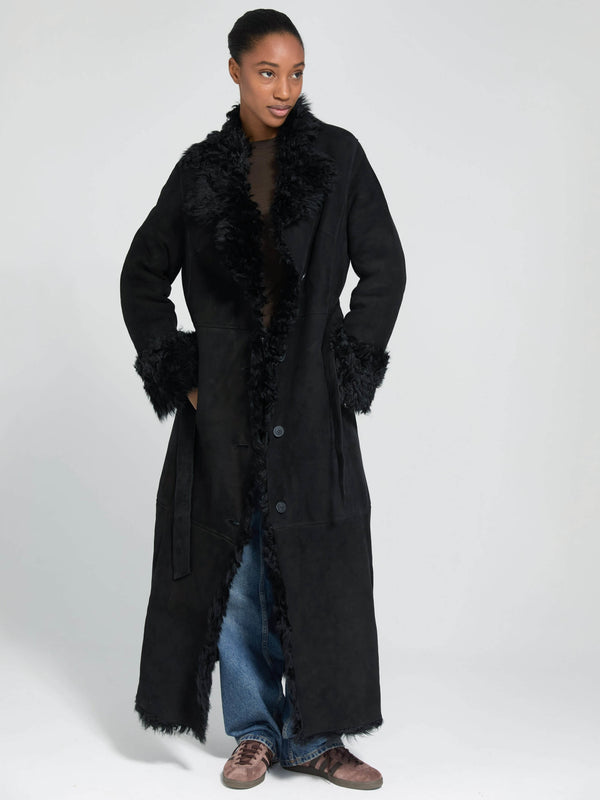A model wears a long black coat with a fluffy collar and cuffs, styled with loose jeans, showcasing MEOTINE's chic design.