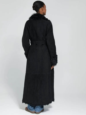 A model showcases a long black coat with a fur collar and cuffs, featuring a belted waist, by MEOTINE.