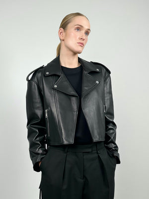A model showcases a stylish black cropped leather jacket with a classic biker design, paired with tailored black trousers. MEOTINE.