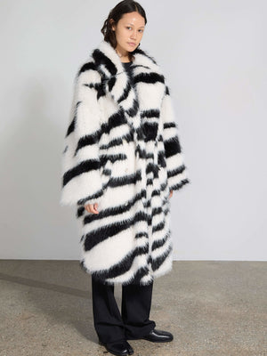 A model showcases a stylish black and white striped faux fur coat by MEOTINE, paired with sleek black trousers.