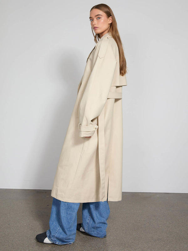 A model showcases a stylish beige trench coat by MEOTINE, paired with wide-leg jeans, set against a minimalist backdrop.