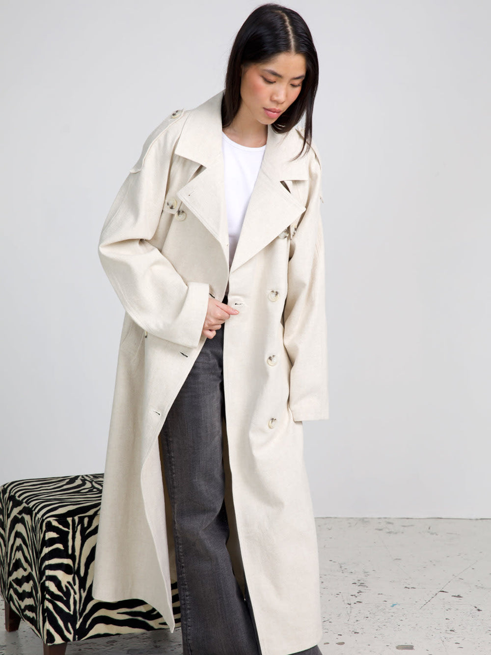 A model wears a stylish beige trench coat by MEOTINE, paired with wide-leg jeans, showcasing a chic and modern look.