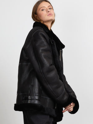 A model showcases a stylish black shearling jacket with a cozy collar, featuring a sleek design by MEOTINE.