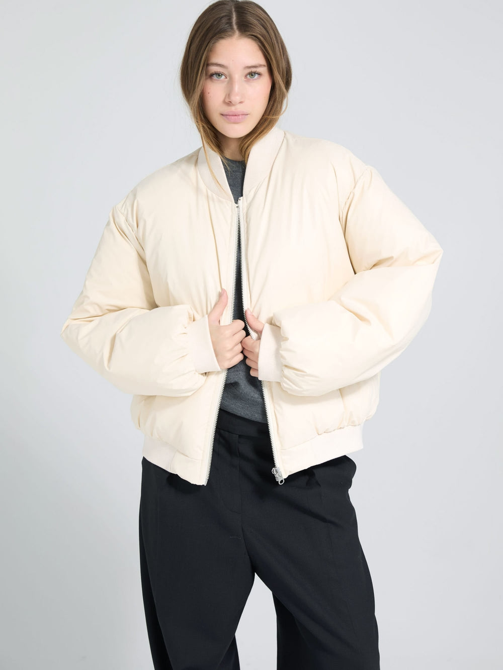 A model wears a cream-colored MEOTINE puffer jacket, styled with a gray top and black pants, against a light background.