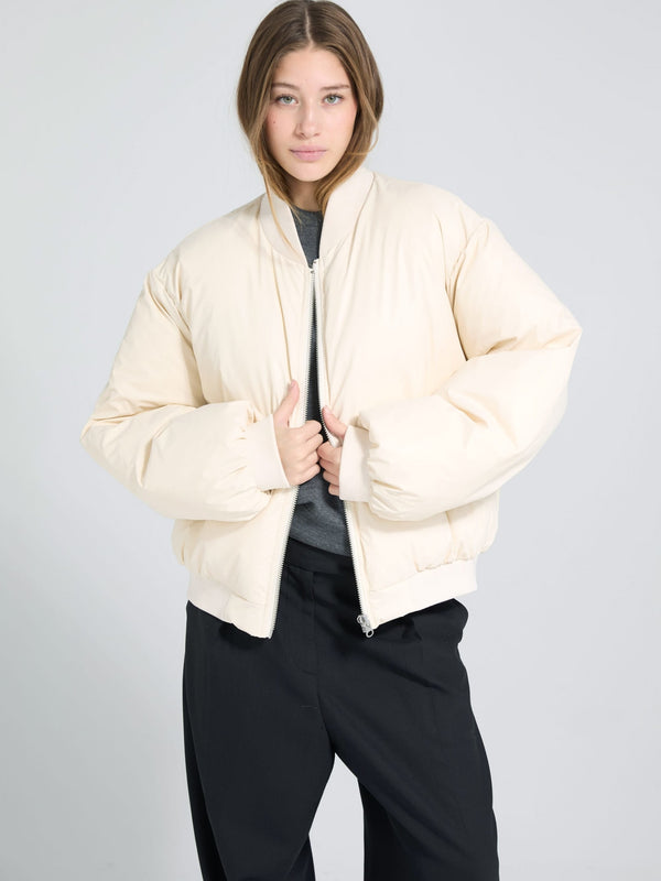 A model wears a cream-colored MEOTINE puffer jacket, styled with a gray top and black pants, against a light background.