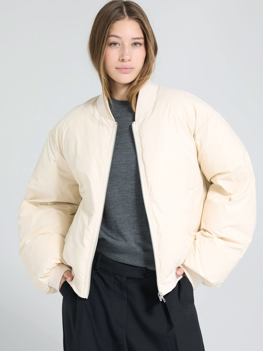 A model wears a cream-colored MEOTINE puffer jacket, styled with a gray top and black pants, against a light background.