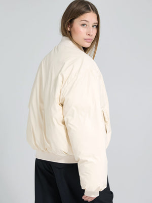 A model showcases a cream-colored bomber jacket from MEOTINE, featuring a relaxed fit and ribbed cuffs, styled with black pants.