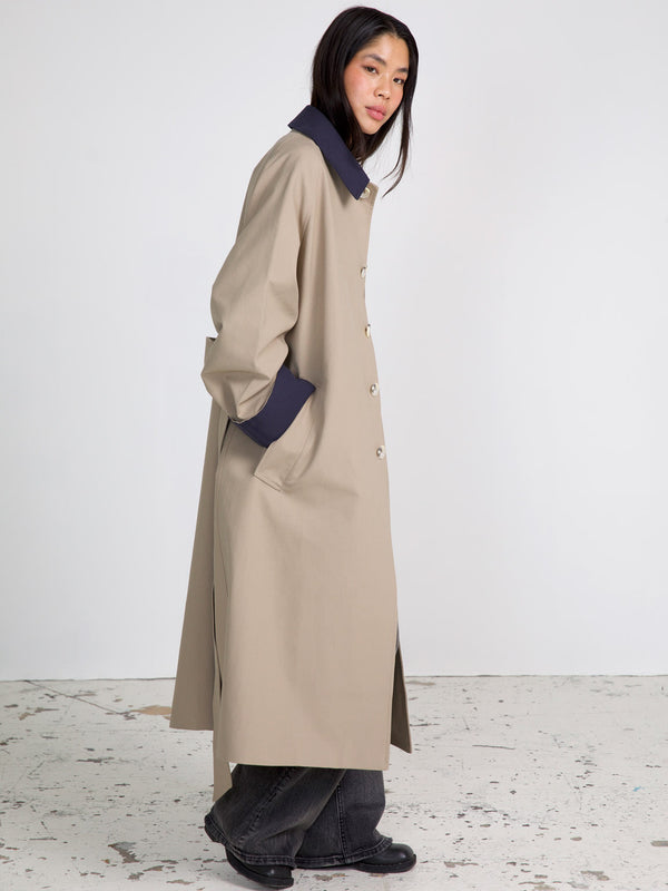 A model showcases a stylish beige long coat with a navy collar, featuring a relaxed fit and side pockets, by MEOTINE.