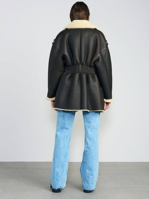 A model wearing a black leather jacket with a cozy shearling collar, paired with light blue flared jeans, showcasing MEOTINE style.