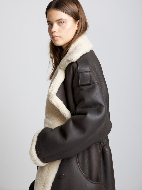 A model showcases a stylish brown shearling coat with a cozy white lining, embodying the chic essence of MEOTINE.