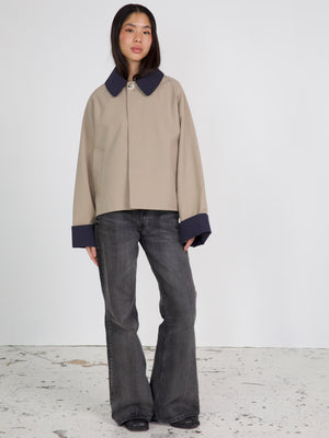 A model wears a beige cropped jacket with a large collar and navy cuffs, paired with flared dark jeans, showcasing MEOTINE's style.