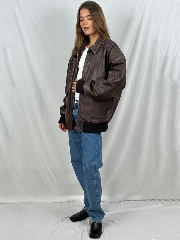 A model showcases a stylish brown leather jacket from MEOTINE, paired with a white shirt and blue jeans, exuding a casual vibe.