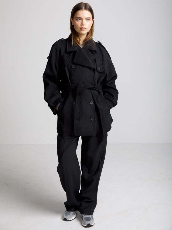 A model wears a stylish black oversized trench coat with a belt, paired with loose black pants and sneakers, showcasing MEOTINE's chic design.